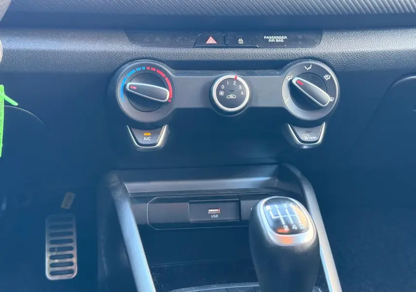 Gros plan sur la console centrale de la KIA RIO rouge grenadine 2022, avec commandes clim et levier de vitesse manuel.