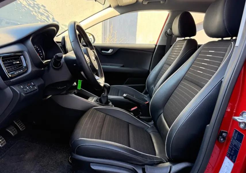 Intérieur côté conducteur d'une KIA RIO rouge grenadine 2022, sièges noirs avec surpiqûres blanches et volant multifonction.