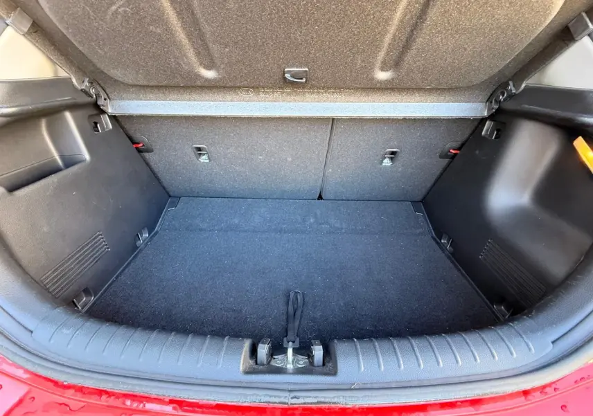 Coffre ouvert vu de l'arrière d'une KIA RIO rouge grenadine, montrant l'espace de chargement vide et les finitions intérieures noires.
