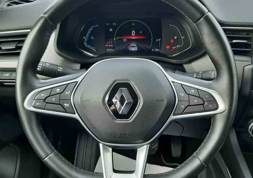 Vue rapprochée du volant noir du Renault Arkana 1.6 E-TECH 145 Intens avec tableau de bord numérique allumé.