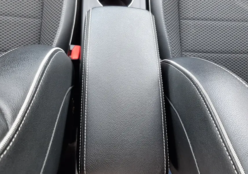 Vue rapprochée de l'accoudoir central noir avec surpiqûres blanches entre deux sièges en tissu gris foncé du Renault Arkana.