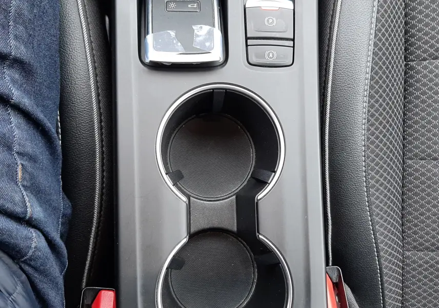 Vue plongeante sur la console centrale noire du Renault Arkana 1.6 E-TECH avec porte-gobelets et commandes électroniques.