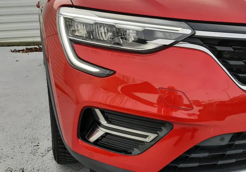 Gros plan sur l'avant gauche du Renault Arkana rouge Flame, mettant en valeur son phare LED et la calandre noire.