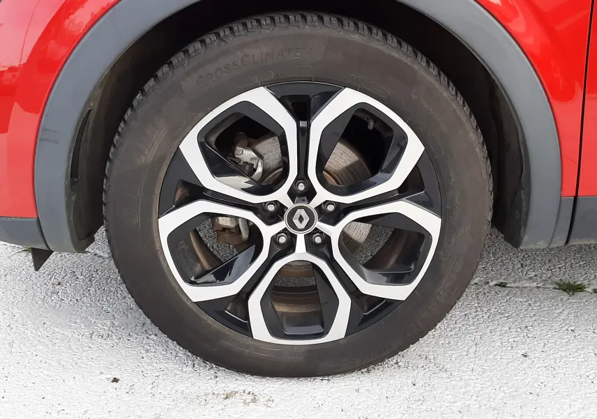 Gros plan sur la roue avant gauche d'un Renault Arkana rouge Flame avec jante alliage noire et argentée.