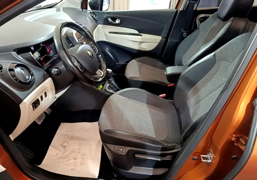Intérieur avant droit du Renault Captur orange 2019, montrant sièges gris, volant cuir et tableau de bord clair.