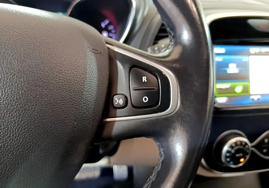 Gros plan sur le volant cuir noir avec commandes vocales du Renault Captur Intens TCe 150 de 2019, tableau de bord flou en arrière-plan.