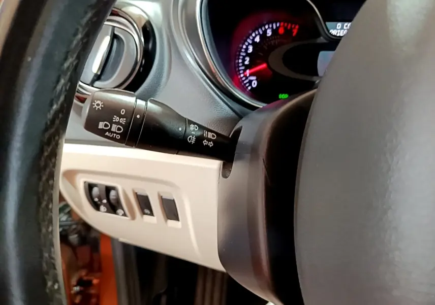 Gros plan sur la commande des phares et le tableau de bord du Renault Captur Intens orange, côté gauche du volant.