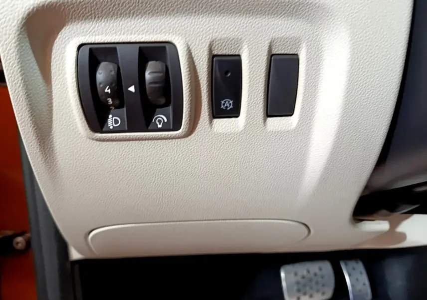 Vue rapprochée des commandes de réglage des phares et du tableau de bord beige du Renault Captur Intens orange 2019.