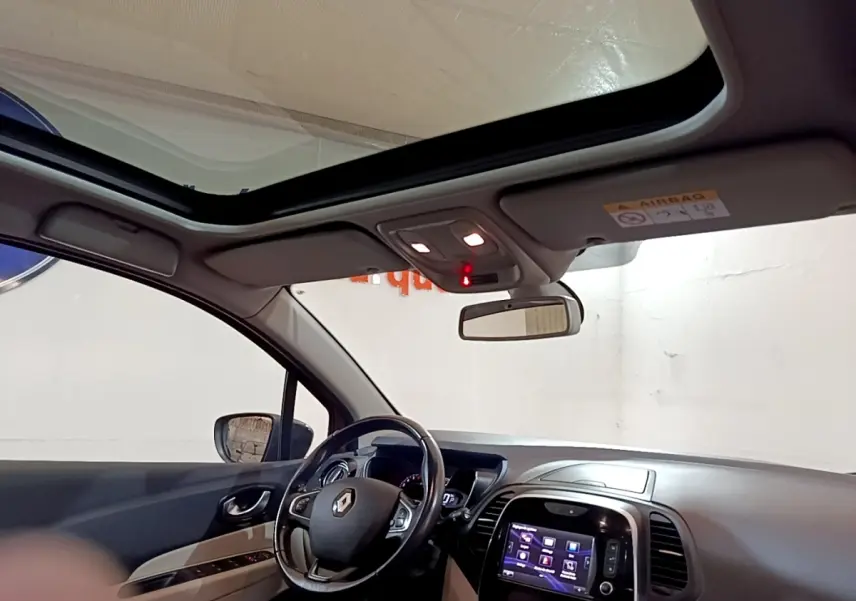 Vue intérieure côté conducteur du Renault Captur Intens 2019, volant cuir, toit panoramique et écran tactile allumé.