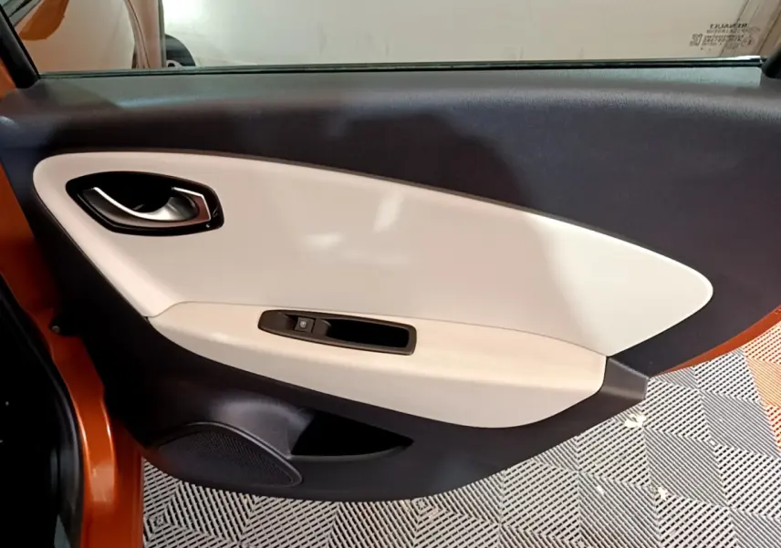 Porte intérieure côté gauche beige et noire du Renault Captur orange 2019, avec poignée et commande de vitre électrique.