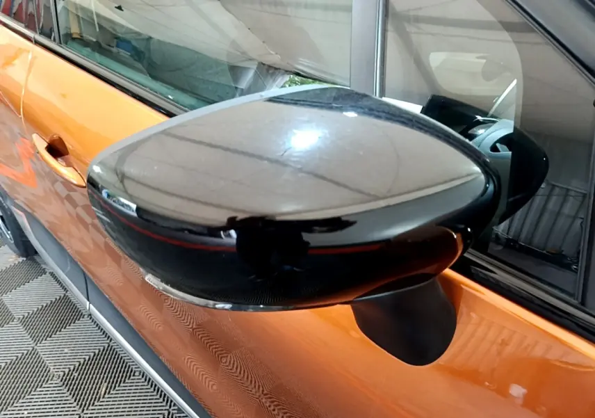 Rétroviseur noir en gros plan côté gauche sur Renault Captur orange, avec reflet intérieur visible.