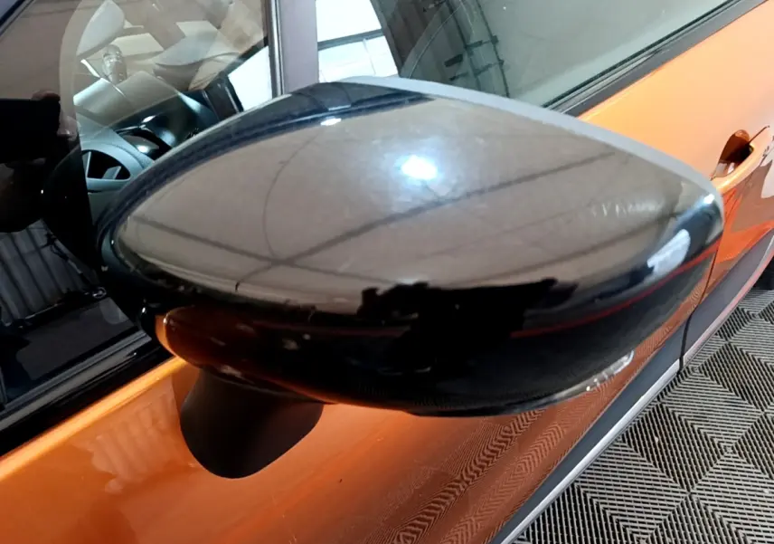 Rétroviseur latéral gauche noir brillant sur Renault Captur orange vu de près côté conducteur.