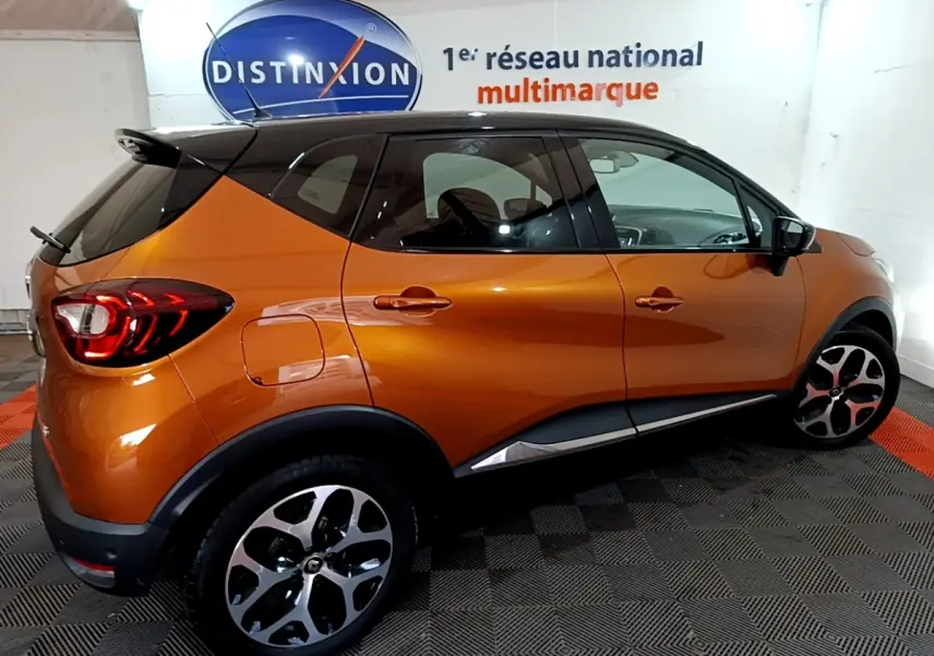 Profil droit du Renault Captur Intens orange 2019 avec toit noir et jantes alliage distinctives dans un showroom.