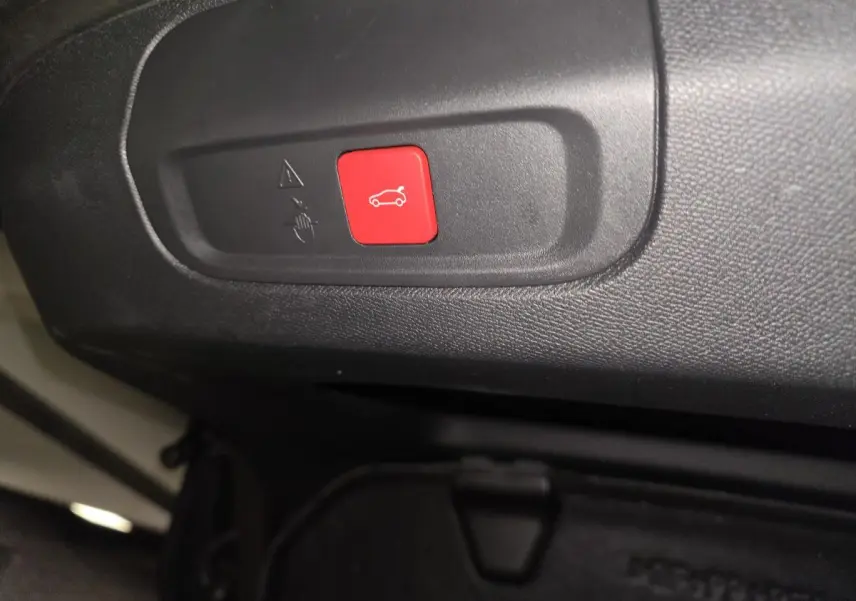 Bouton rouge d'ouverture du coffre sur panneau intérieur noir d'une Peugeot 408 2024 hybride rechargeable.
