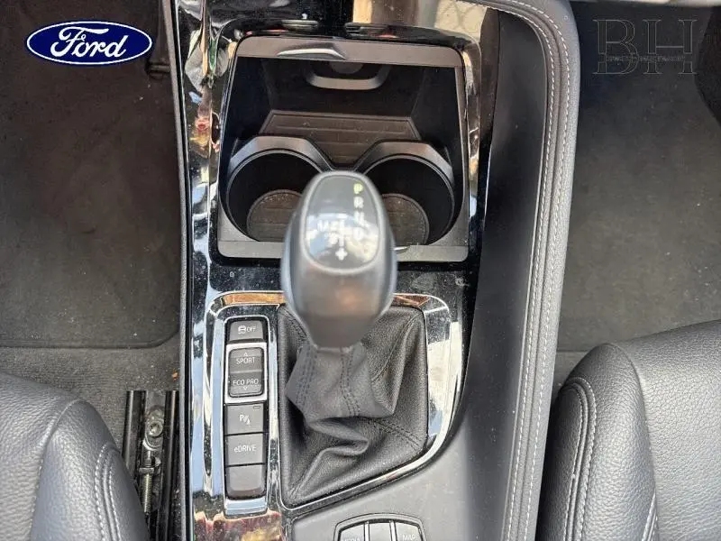 Vue plongeante sur la console centrale noire avec levier de vitesse automatique et boutons de modes de conduite BMW X1 Saphirschwarz.