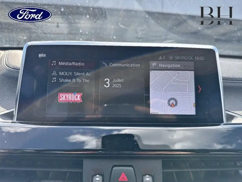Écran central du tableau de bord de BMW X1 xDrive25e 2021 affichant radio Skyrock, date et navigation.