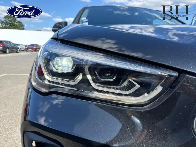 Gros plan sur le phare avant gauche du BMW X1 xDrive25eA 2021 en couleur Saphirschwarz, avec détails LED visibles.