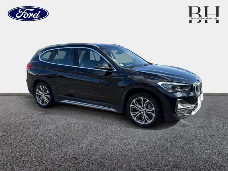 BMW X1 xDrive25e saphirschwarz vue 3/4 avant droit, jantes alliage et lignes dynamiques visibles.
