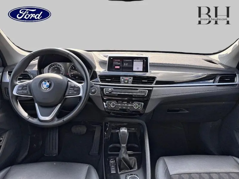 Vue intérieure avant du tableau de bord et volant cuir multifonction d'une BMW X1 xDrive25eA 2021 en noir.