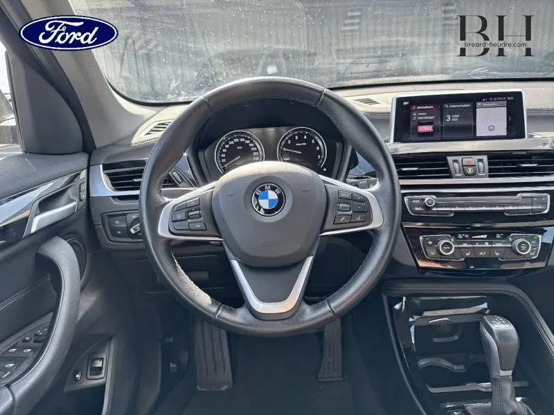 Vue intérieure centrée sur le volant cuir noir et le tableau de bord digital d'une BMW X1 xDrive25eA 2021.