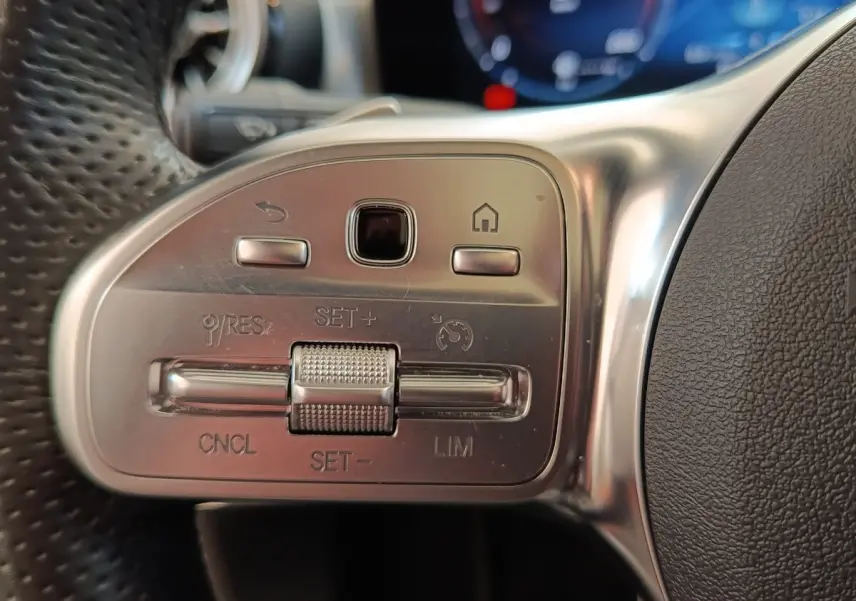 Gros plan sur les commandes en aluminium et cuir du volant multifonctions de la Mercedes Classe A blanche, côté gauche.