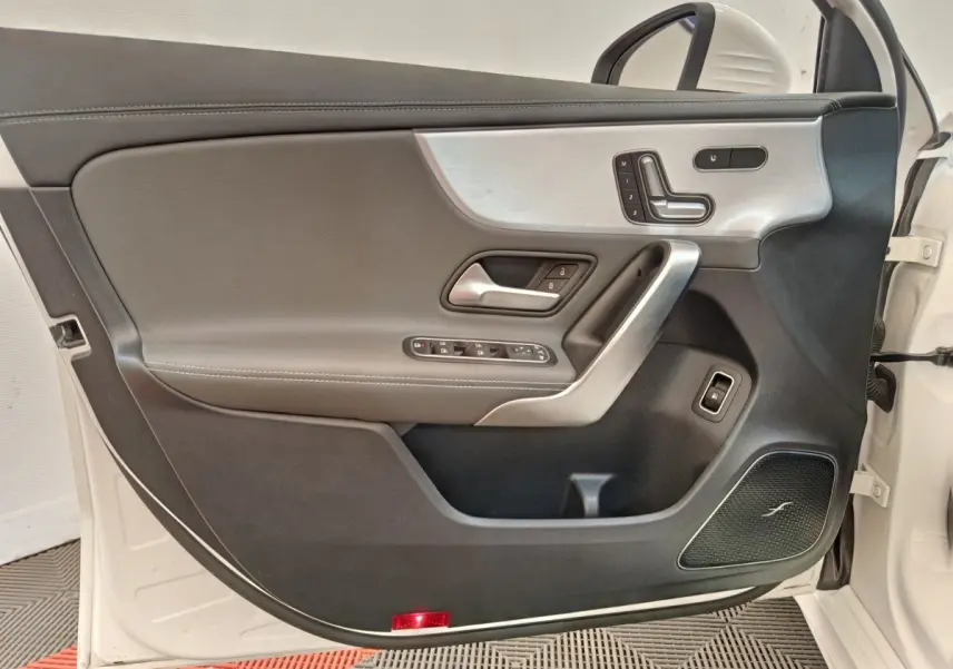 Vue intérieure de la porte avant gauche blanche d'une Mercedes Classe A 250 e AMG Line avec garniture cuir et insert alu.