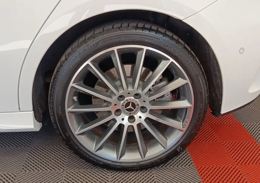 Gros plan sur la roue avant droite avec jante alliage gris et logo Mercedes sur une Mercedes Classe A blanche.