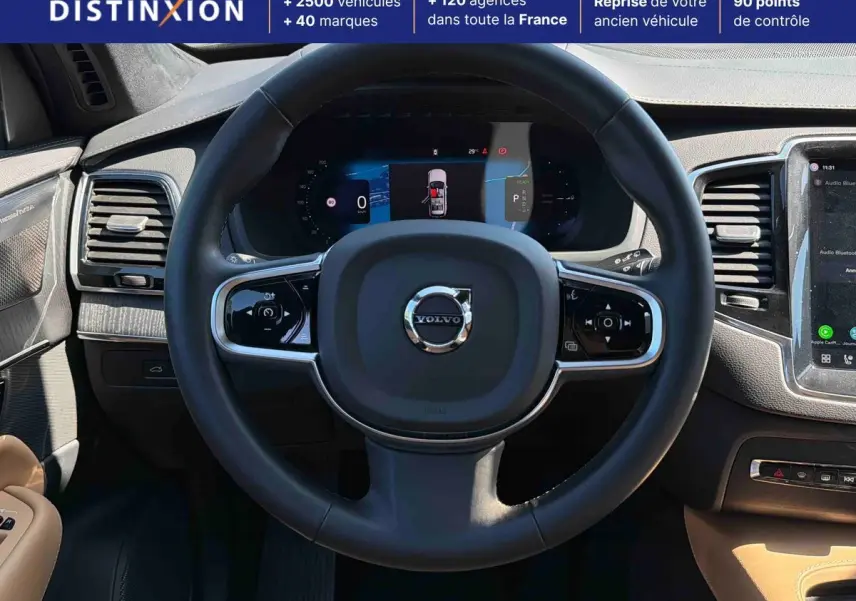 Vue intérieure centrée sur le volant cuir noir et le tableau de bord digital du Volvo XC90 hybride 2024.