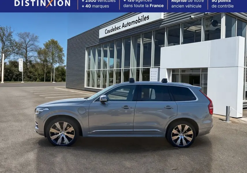 Vue de profil côté gauche d'un Volvo XC90 gris 2024 hybride rechargeable avec jantes alliage et barres de toit.
