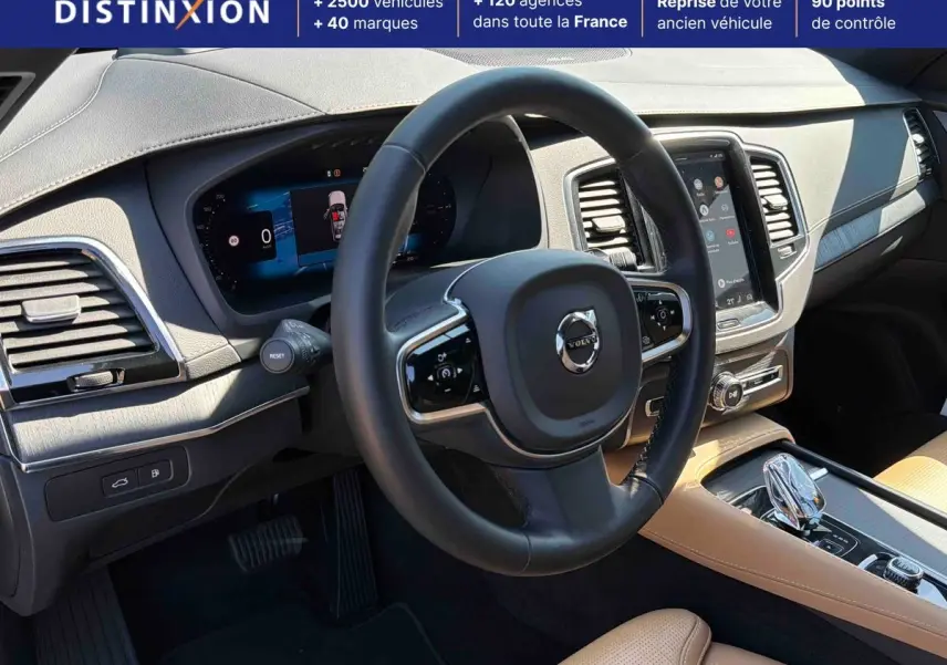 Vue intérieure du tableau de bord et volant noir du Volvo XC90 2024 avec écran tactile vertical et sellerie cuir beige.