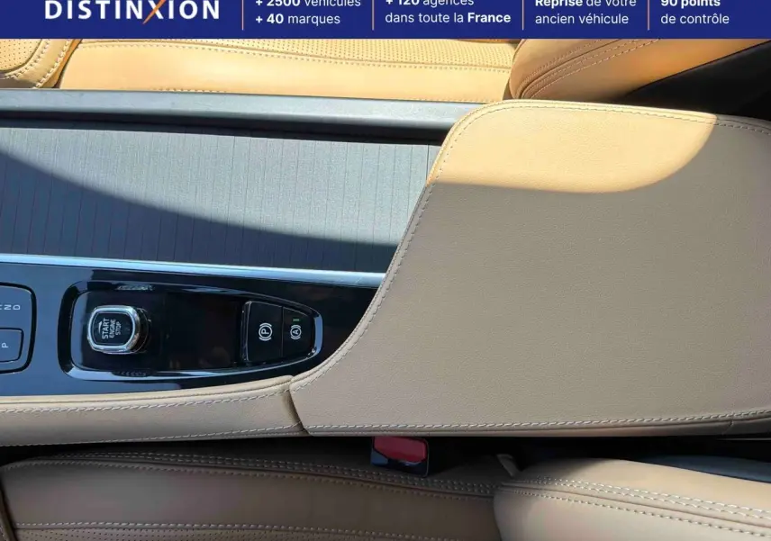 Gros plan sur la console centrale beige du Volvo XC90 2024 avec bouton start/stop et commandes de frein à main.