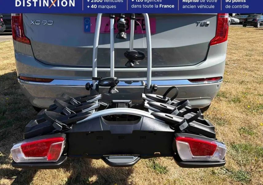 Vue arrière d'un Volvo XC90 gris avec porte-vélos fixé à l'attelage, sur un terrain herbeux.