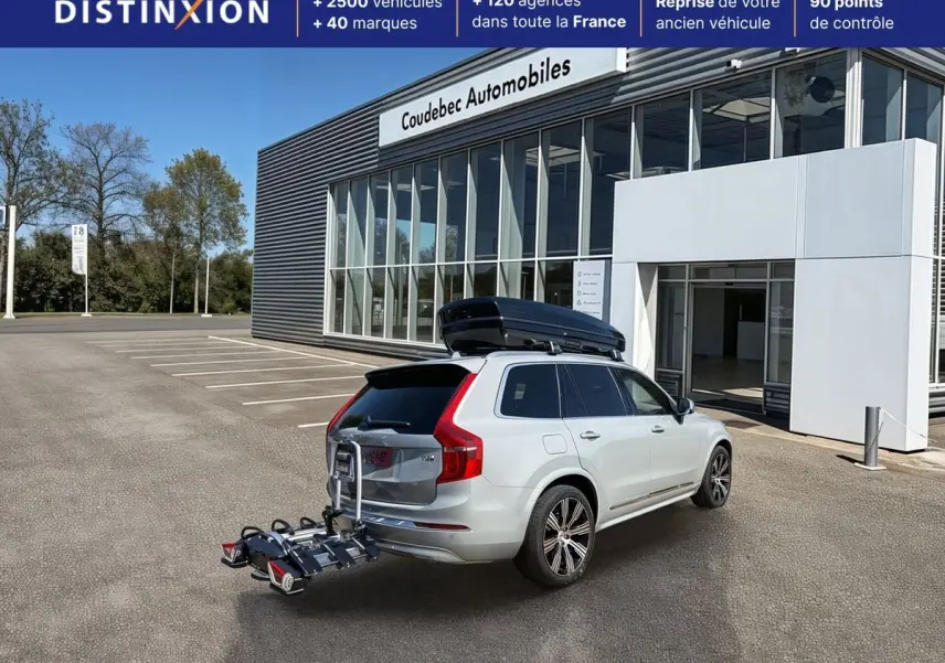 Vue 3/4 arrière droite d’un Volvo XC90 gris avec coffre de toit noir et porte-vélos fixé à l’attelage.