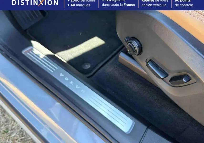 Détail du seuil de porte côté conducteur gris avec inscription Volvo et commandes électriques du siège cuir beige.