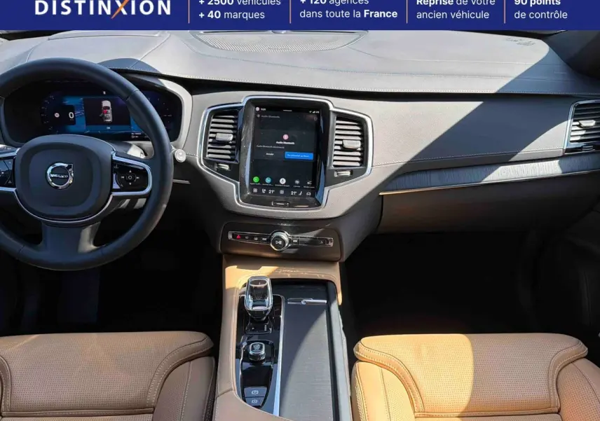 Vue intérieure avant du Volvo XC90 2024 avec tableau de bord gris et sellerie cuir beige perforé.