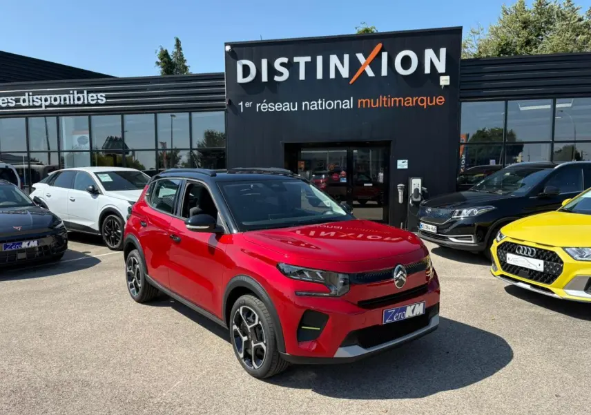 Citroën C3 2025 rouge Elixir avec toit noir, vue 3/4 avant droit, stationnée devant un concessionnaire multimarque.