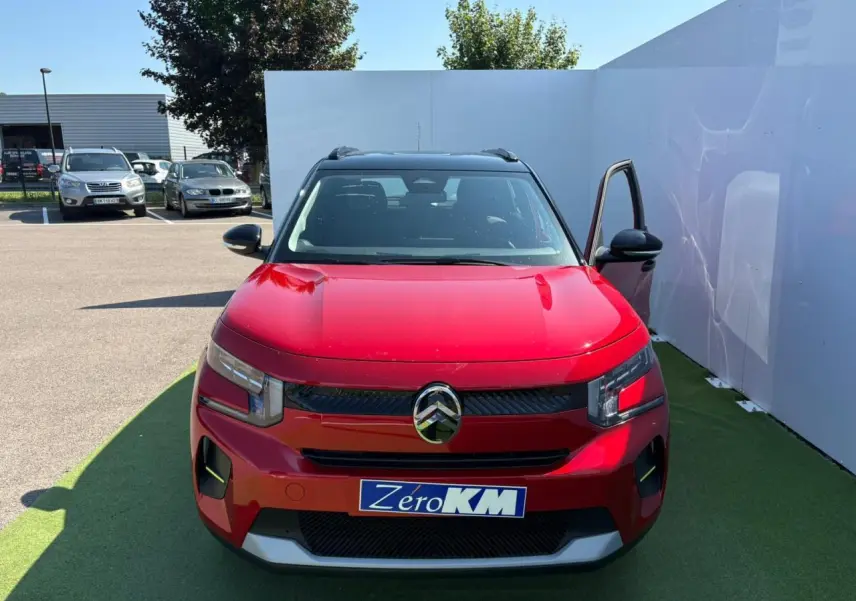 Citroën C3 IV rouge Elixir avec toit noir, vue de face, porte avant droite ouverte sur parking.