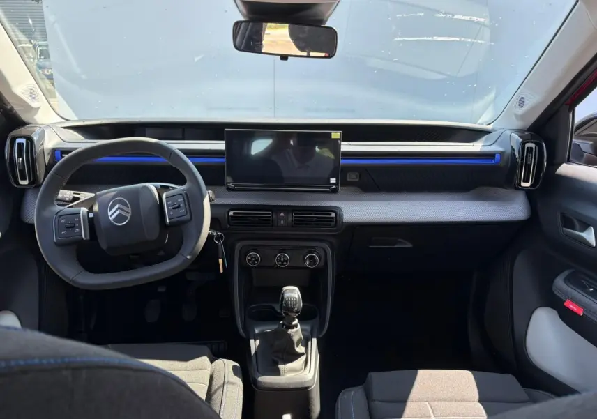 Vue intérieure avant de la Citroën C3 2025 avec tableau de bord gris, écran tactile et volant multifonction noir.