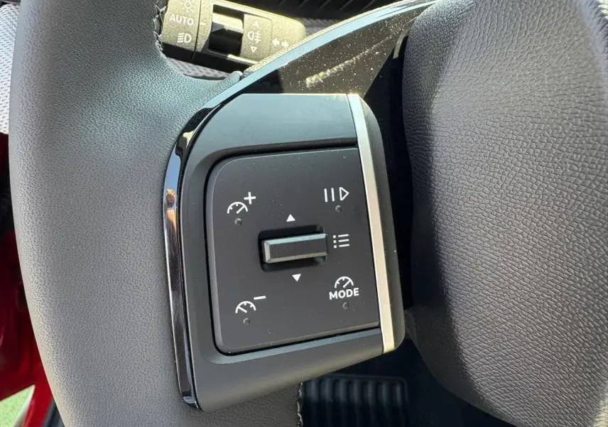 Gros plan sur les commandes de régulateur de vitesse au volant d'une Citroën C3 rouge Elixir toit noir.