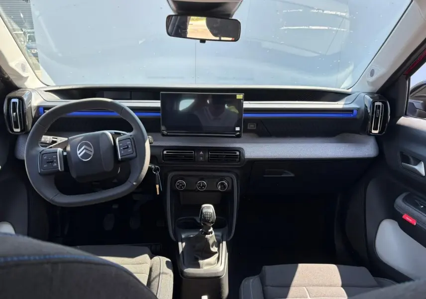 Vue intérieure avant de la Citroën C3 2025 rouge Elixir, tableau de bord avec écran tactile et volant multifonctions noir.