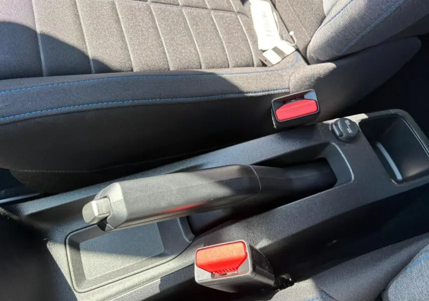 Vue rapprochée de la poignée de frein à main et des ceintures rouges entre les sièges avant noirs à surpiqûres bleues d'une Citroën C3 2025.
