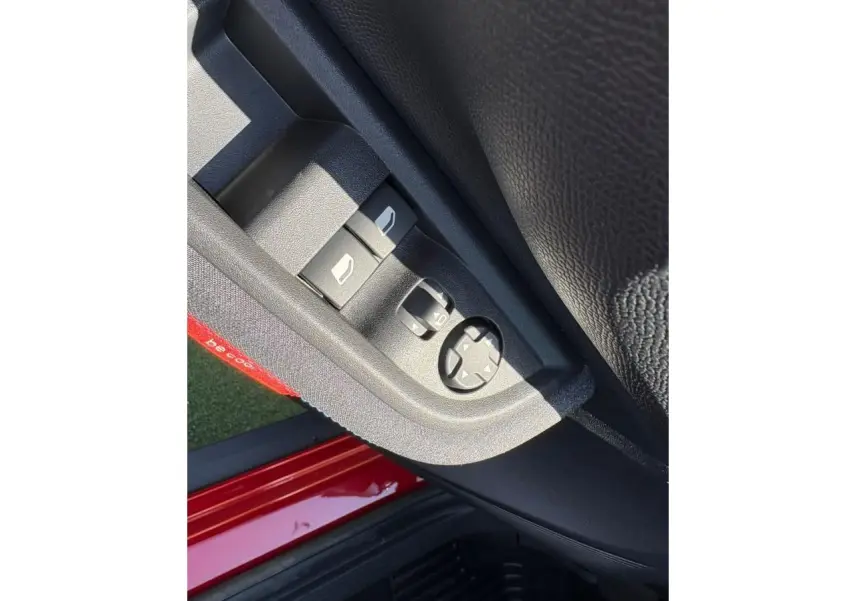 Gros plan sur les commandes de lève-vitres et rétroviseurs côté gauche d'une Citroën C3 rouge Elixir avec intérieur noir.