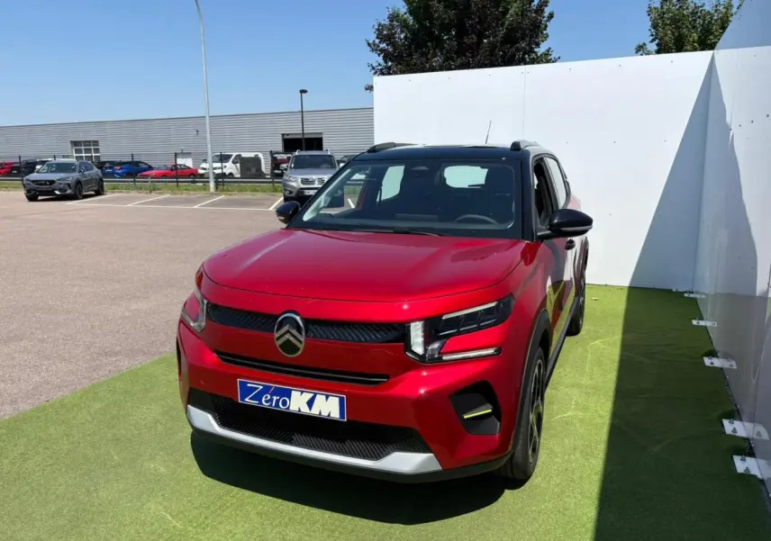Citroën C3 2025 rouge Elixir avec toit noir, vue 3/4 avant sur parking, plaque Zéro KM visible.