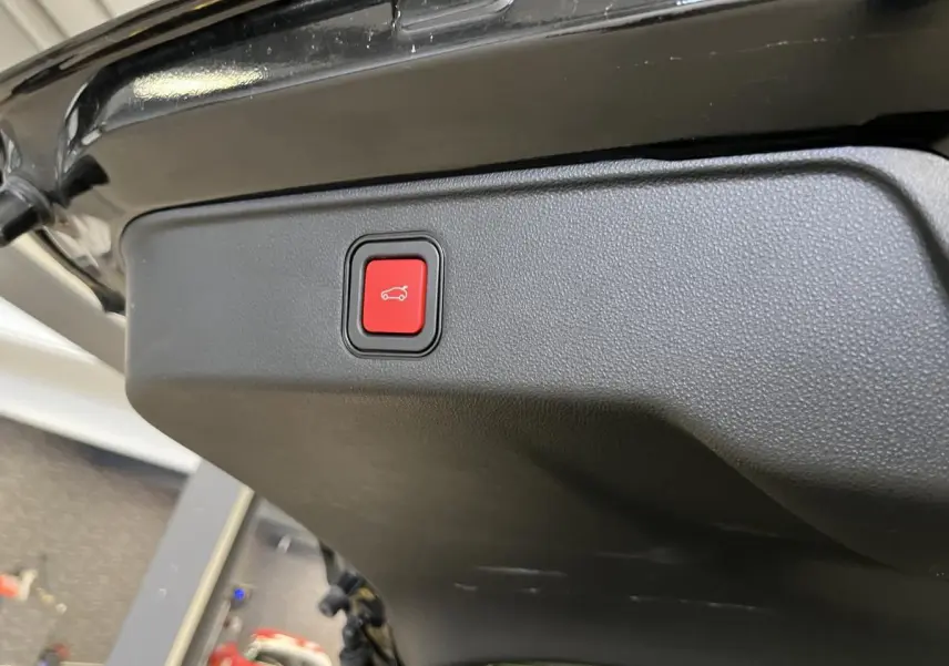 Bouton rouge d'ouverture électrique du hayon sur la partie intérieure du coffre d'une FIAT 600 noire 2024.