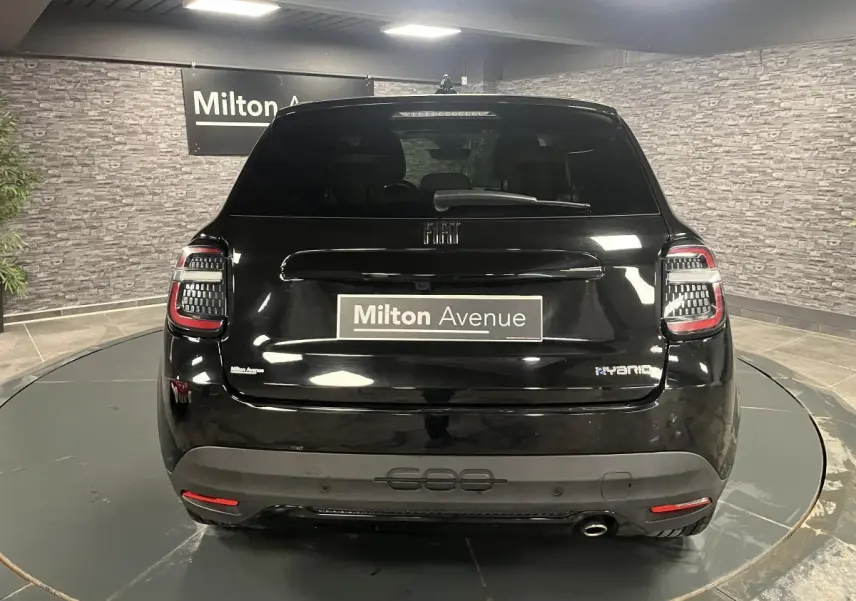 Vue arrière d'une FIAT 600 noire hybride 2024 avec logo chromé et canule d'échappement visible en intérieur showroom.