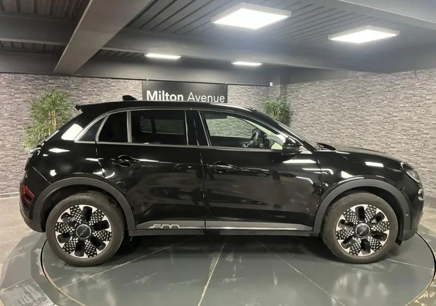 Profil côté gauche d'un FIAT 600 1.2 Hybrid noir brillant avec jantes alliage 18'' diamantées dans un showroom.