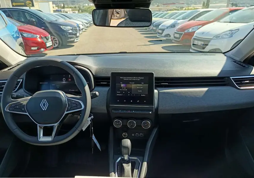 Vue intérieure avant du tableau de bord et volant de la Renault Clio 2025 gris schiste avec écran tactile central et boîte auto.
