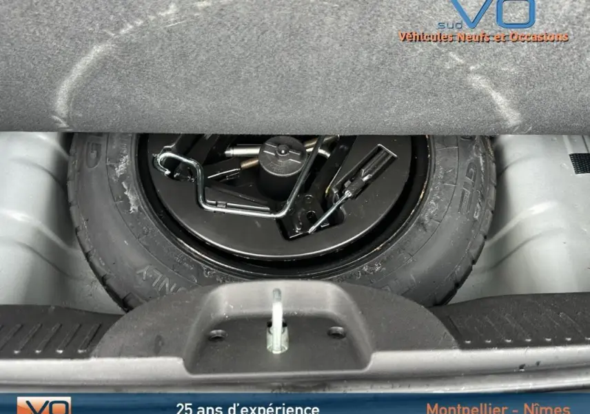 Roue de secours noire avec outils de changement visible dans le coffre d'une FIAT 500C 2024 noire hybride.