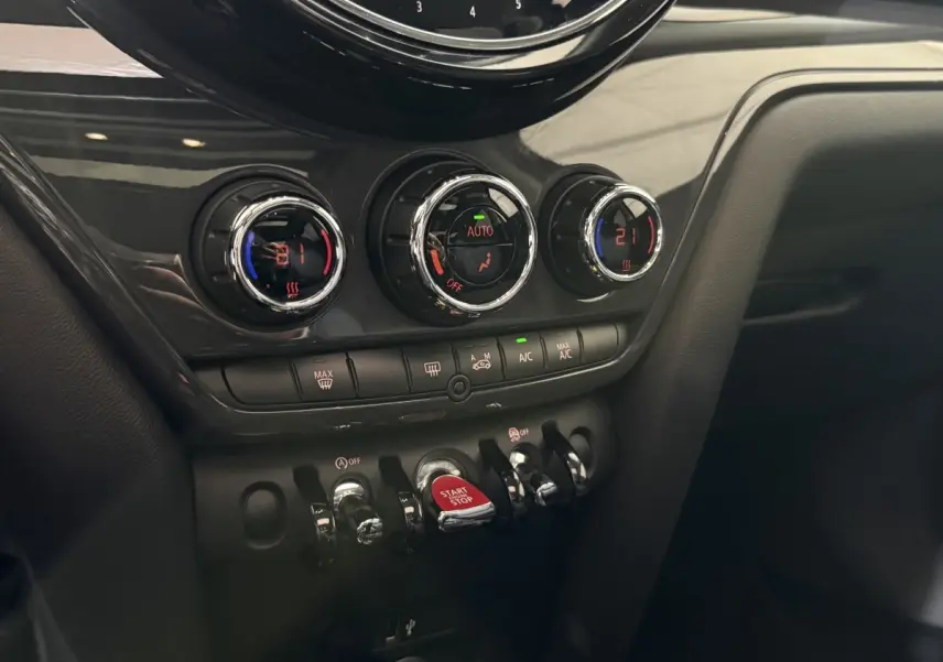 Vue rapprochée du tableau de bord noir de la MINI Countryman 2020, montrant les commandes de climatisation et le bouton start/stop rouge.