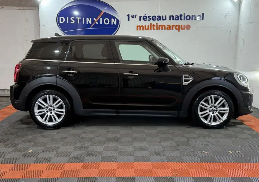 Profil côté gauche d'une MINI Countryman noire 2020, avec jantes alliage et toit noir dans un showroom.